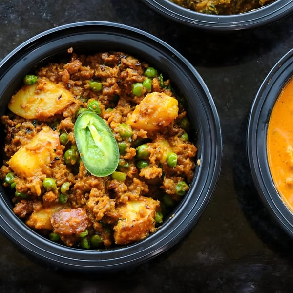 A close-up of Indian Aloo Keema with potatoes, peas, and ground meat in a black bowl.