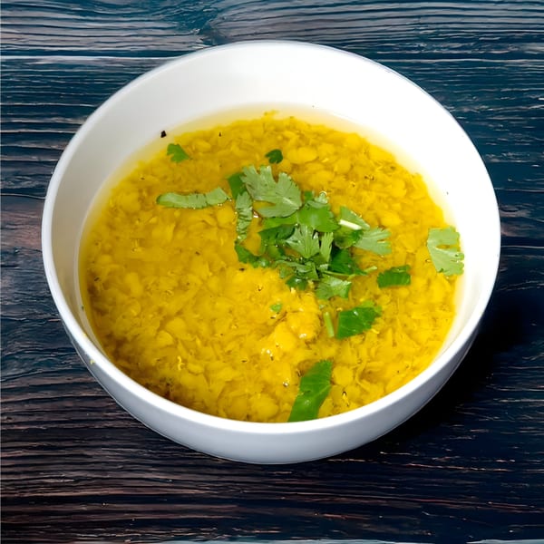 A white bowl of yellow Indian lentil soup, dal, garnished with fresh green cilantro on a dark wooden surface.