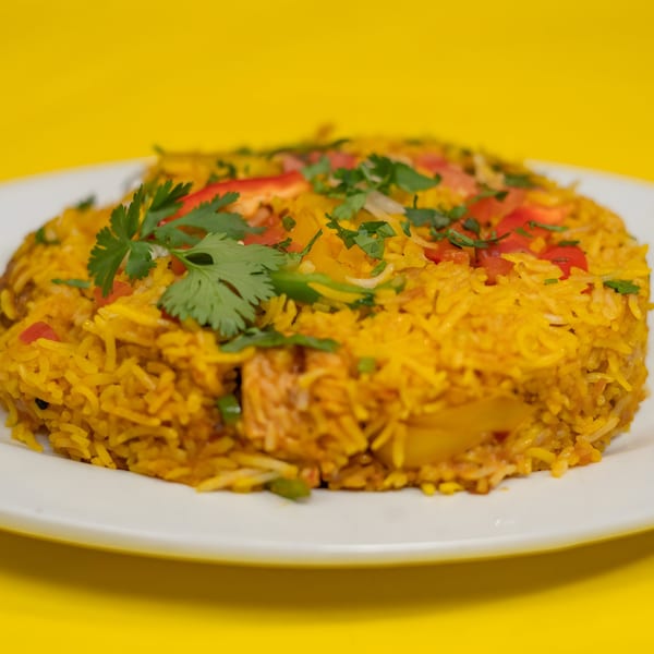 A vibrant Indian biryani dish, garnished with fresh cilantro and diced vegetables, on a white plate.